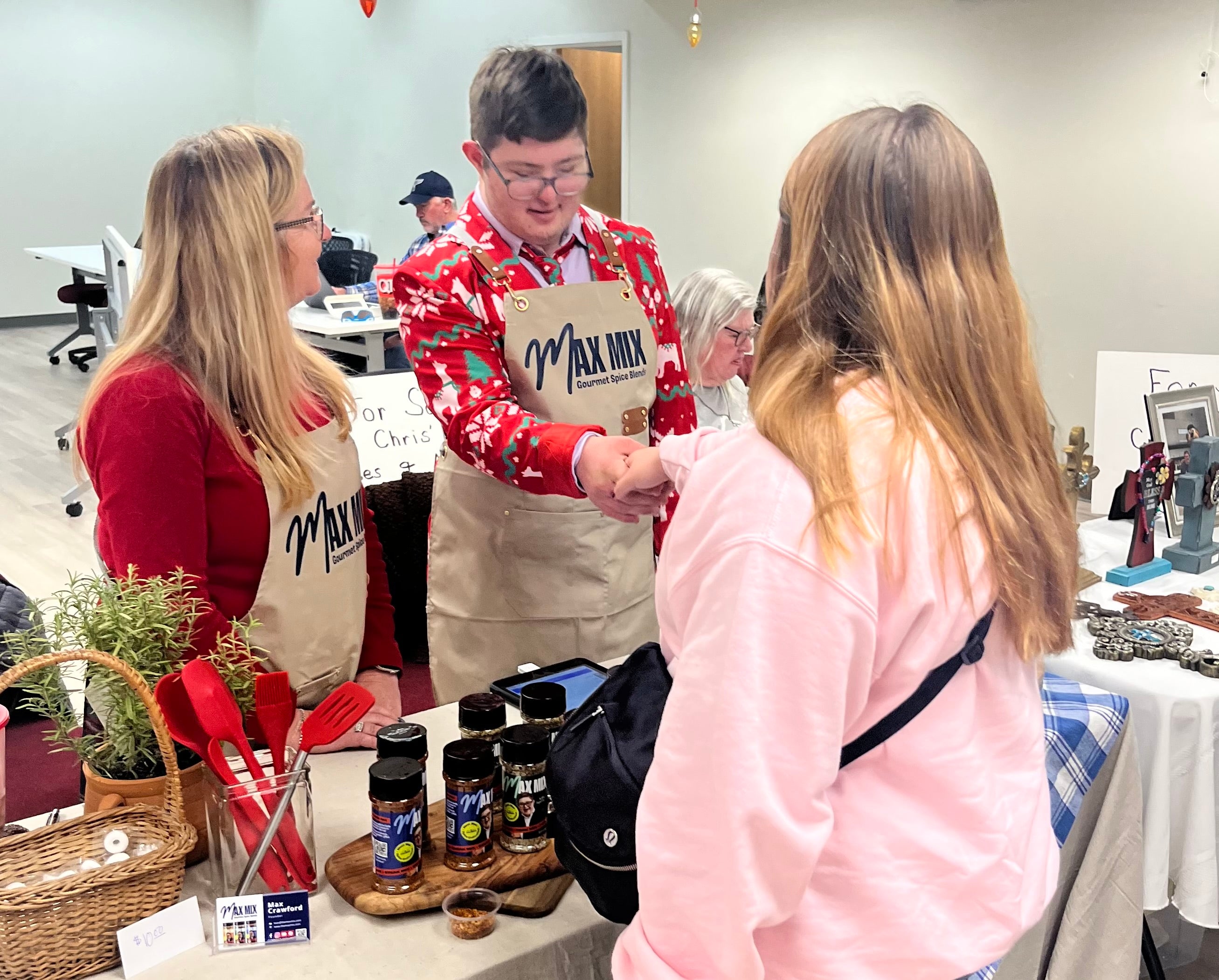 A picture of Max at a product demo with his mother, wearing a Max Mix branded apron and shaking hands with a customer.