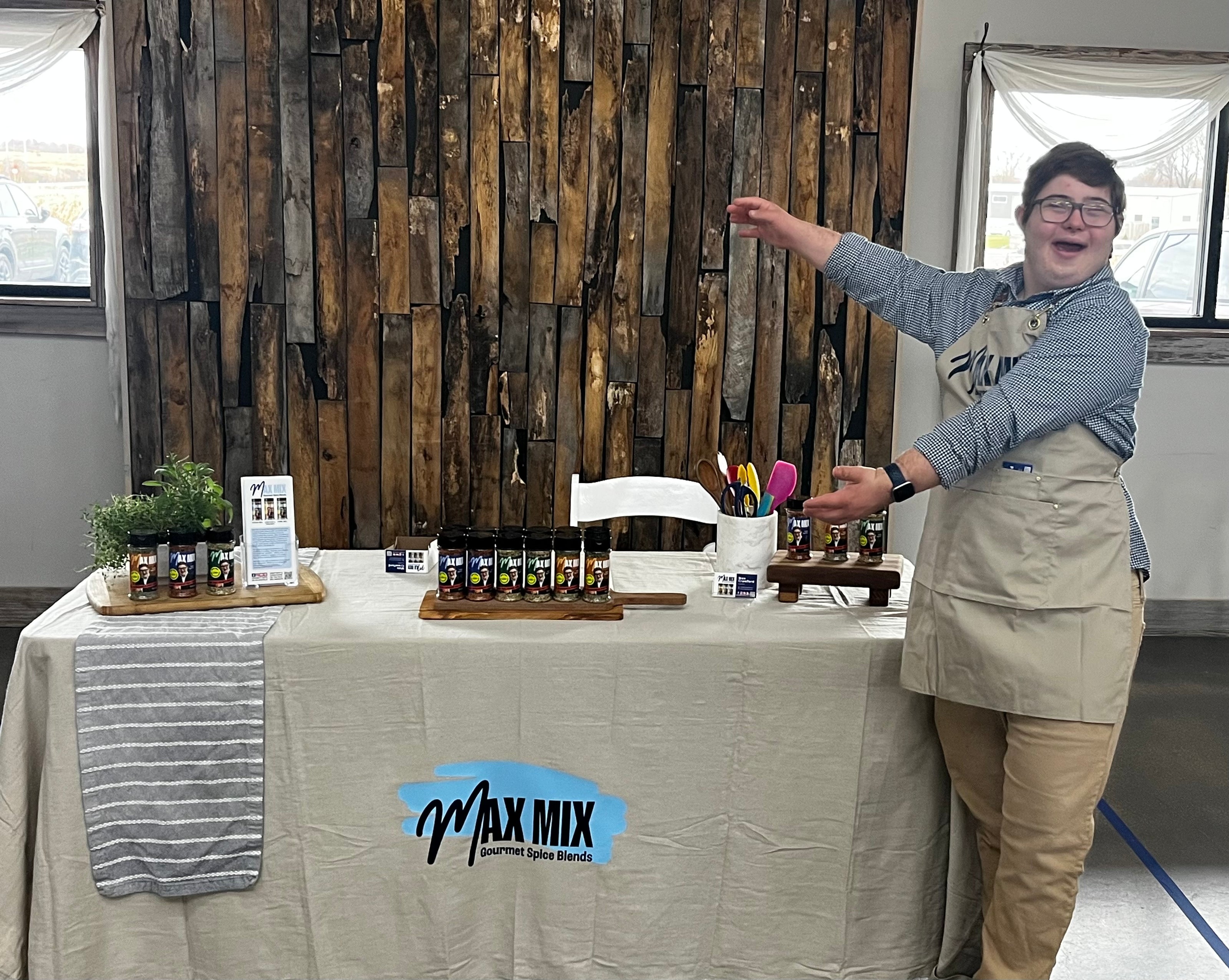 A picture of Max at a product demo, wearing a Max Mix branded apron and proudly presenting the table of his spice mix shakers.