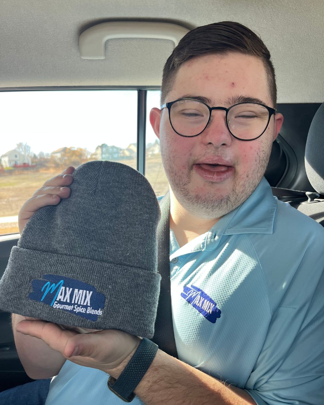 A picture of Max Mix founder Max, holding up a grey beanie with company logo, and smiling into the camera.