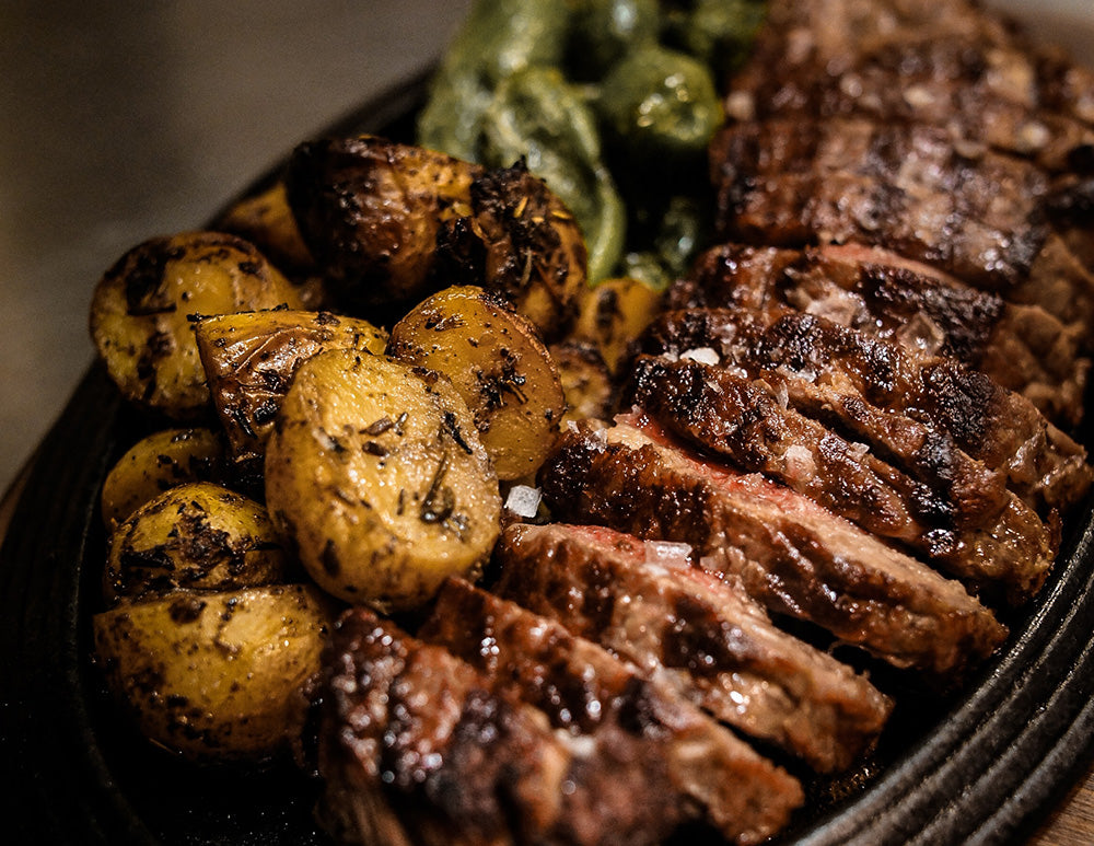 A serving dish full of carved steak, potatoes, and green vegetables.