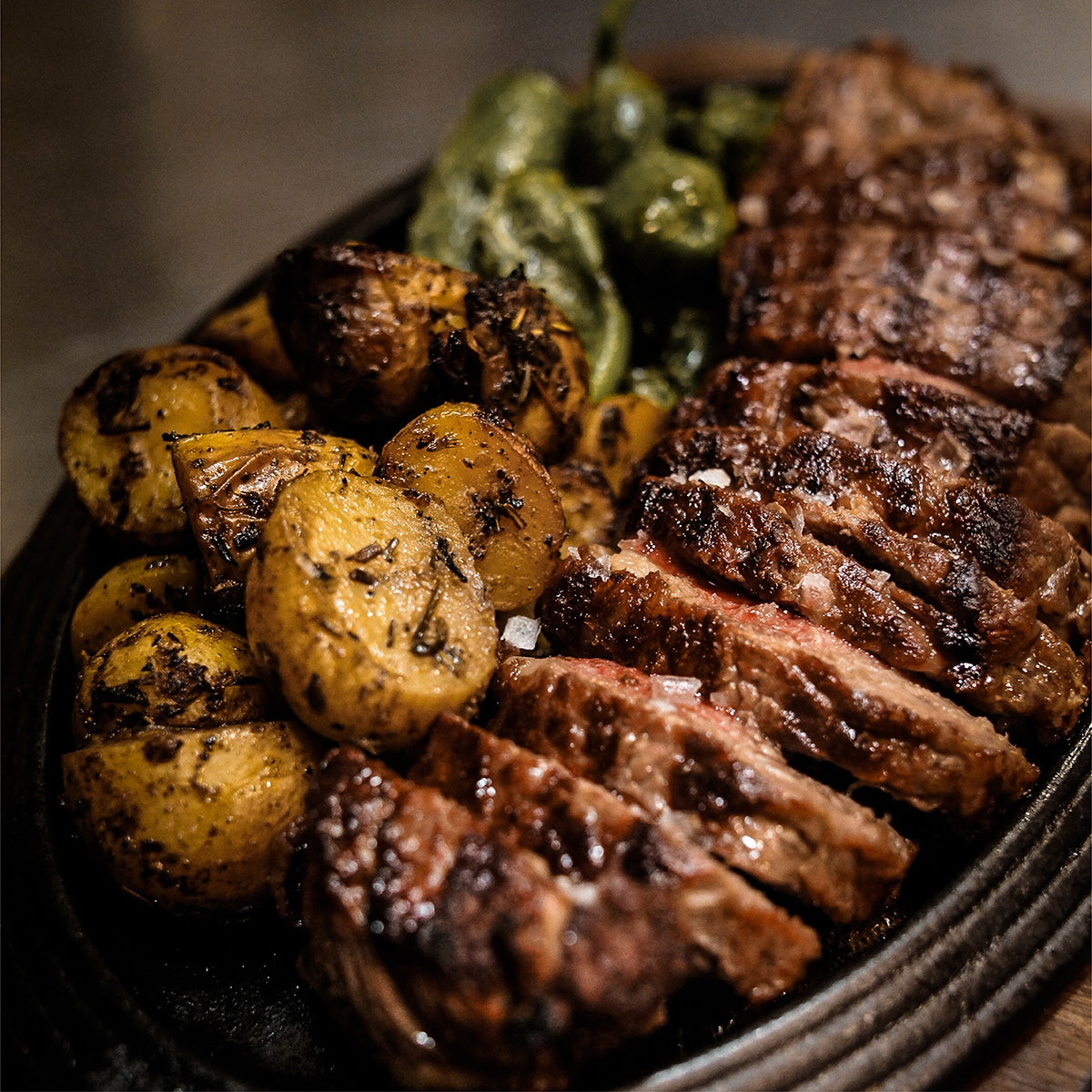 A serving dish full of carved steak, potatoes, and green vegetables.