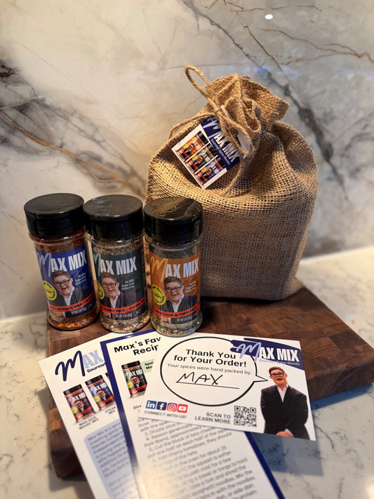 Three bottles of Max Mix product (Steak Mix, Pork Mix, Chicken & Fish Mix), arranged on a wooden cutting board with a burlap drawstring bag and printed cards, set against a marble-patterned background.